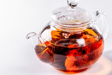 Tea in a glass teapot with a blooming large flower. Teapot with exotic green tea on white background