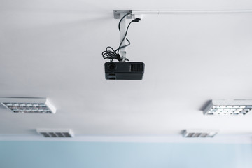 Black projector on a ceiling in a classroom.