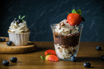 Delisious cakes with cream and berries an the dark stone background.