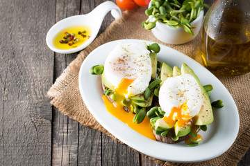 Avocado toast, cherry tomato on wooden background. Breakfast with toast avocado, vegetarian food, healthy diet concept. Healthy sandwich with avocado and poached eggs.