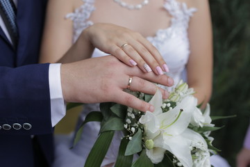 Obraz na płótnie Canvas newlyweds demonstrate wedding rings on hands over a bouquet of white lilies
