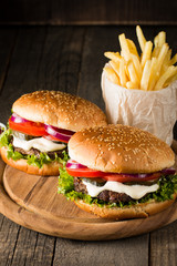 Close-up photo of home made hamburger with beer made of beef, onion, tomato, lettuce, cheese and spices. Fresh burger closeup on wooden rustic table with potato fries and chips.