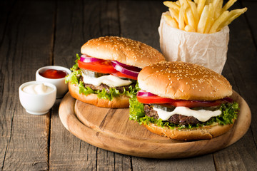 Close-up photo of home made hamburger with beer made of beef, onion, tomato, lettuce, cheese and spices. Fresh burger closeup on wooden rustic table with potato fries and chips.