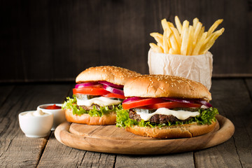 Close-up photo of home made hamburger with beer made of beef, onion, tomato, lettuce, cheese and spices. Fresh burger closeup on wooden rustic table with potato fries and chips.
