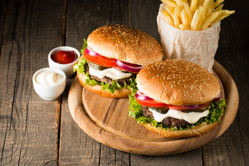 Close-up photo of home made hamburger with beer made of beef, onion, tomato, lettuce, cheese and spices. Fresh burger closeup on wooden rustic table with potato fries and chips.