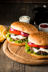 Close-up photo of home made hamburger with beer made of beef, onion, tomato, lettuce, cheese and spices. Fresh burger closeup on wooden rustic table with potato fries and chips.