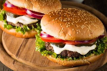 Close-up photo of home made hamburger with beer made of beef, onion, tomato, lettuce, cheese and spices. Fresh burger closeup on wooden rustic table with potato fries and chips.