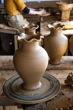 Female artisan sitting in her creative workshop using her hands to shape a wet piece of clay turning on a pottery wheel