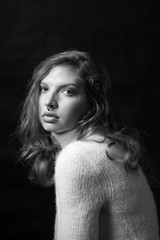 Black and white fashion portrait of beautiful girl with curly hair and big lips in white sweater posing in studio in front of black background. Art photo portrait