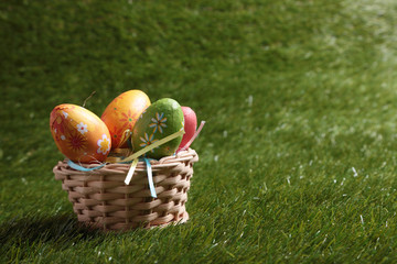 A bunch of colorful Easter eggs in a wicker basket on green grass