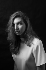 Black and white fashion portrait of beautiful model woman with luxurious curly hair in elegant white blouse posing in studio in front of black background. Art photo portrait