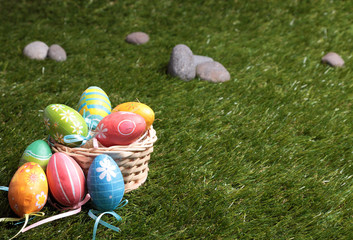 A bunch of colorful Easter eggs in a wicker basket on green grass in a park