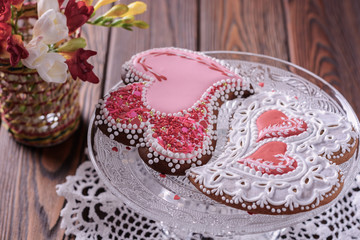A pair of beautiful home-made gingerbreads for a wedding celebration or Valentine's day next to flowers on a glass cake stand on a wooden table, closeup
