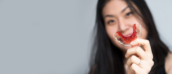 Portrait of beautiful Asian patient woman holding orthodontic retainers in dental clinic, Smiling Girl Holding blue Retainer, Braces for Teeth. Orthodontics Dental Theme, Methods of Teeth Correction