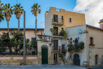 Fototapeta na wymiar Typical italian house with greenery balconies and palm trees nearby, island Ortigia, Syracusa, Sicily, Italy
