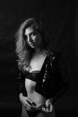 Obraz na płótnie Canvas Black and white fashion photo of beautiful sexy woman with luxurious curly hair in elegant jacket and lingerie posing in studio in front of black background. Perfect model body