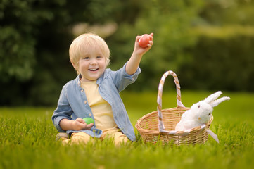Charming little boy hunting for easter egg in spring park on Easter day.