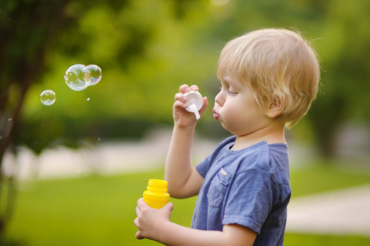 Cute little boy blowing soap bubbles in beautiful summer park.