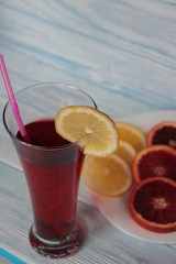 A glass of juice, red orange and  lemon on a platter.