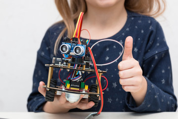 Cute little girl codes a metal car robot and an electronic board. Robotics and electronics. Laboratory. Mathematics, engineering, science, technology, computer code. STEM education. DIY. AI.