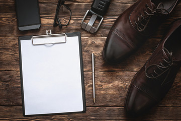Business to do list. Blank paper sheet, mobile phone, glasses, belt and a elegant shoes on a brown wooden floor background with copy space.