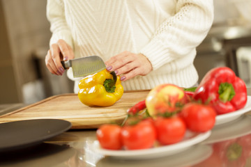 Cropped shot of a woman chopping yellow paprika pepper, while cooking at the kitchen. Housewife preparing vegetables for salad. Healthy lifestyle, eating, food, dieting concept