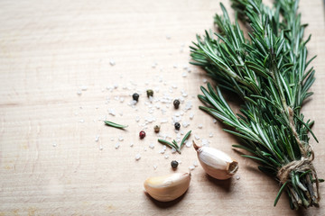 Fresh rosemary herb, garlic and spices on a light board top view copy space.