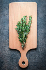 Fresh rosemary herb on a wood board on a dark background top view copy space