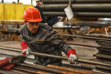 Horizontal shot of a handsome young warehouse manager organizing steel supplies wearing protective hardhat and uniform, copy space. Heavy industry, construction, engineering concept