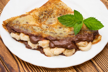Crepes with bananas and cream on a wooden background