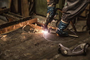Cropped shot of a professional metalworker in protective uniform welding steel sheets with plasma cutting machine, copy space. Metalworking, heavy industry, export concept