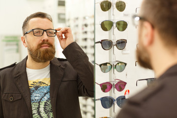 Close up shot of a bearded handsome man shopping for new glasses. Handsome male customer trying on...