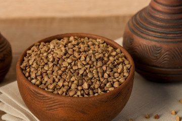 Dry buckwheat in brown clay bowl on wooden table. gluten free grain for healthy diet