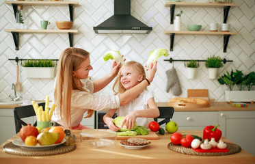 Mother with her daughter in kitchen preparing healthy food with fresh vegetables