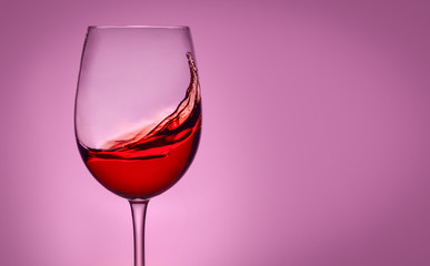 Glass of red wine on pink isolated background. Splashes and reflection.