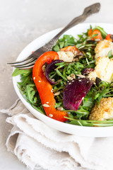 Salad with arugula, roasted vegetables (cauliflower, red bell pepper and onion) and seeds. Healthy food. Light grey concrete background. Copy space.