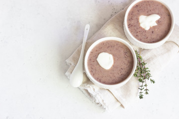 Cream soup with cauliflower and red bean served with sour cream and thyme. Light grey concrete background. Copy space. Comfort food.