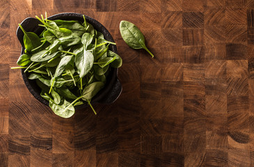 Fresh baby spinach leaves in bowl on butcher board