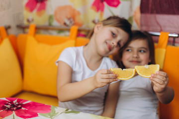 Two little preschool children girls playing at home together with orange. Cheerful happy little girls friends. Sisterhood, childhhod, happiness concept