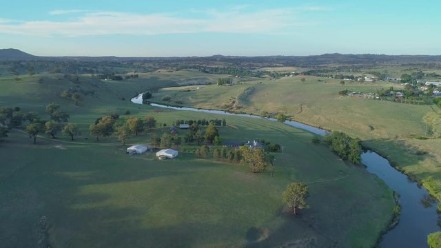 Forward flight over meadows and pastures near winding river at sunset in Australia