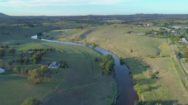 Backward flight over winding river among meadows and pastures at sunset. New South Wales, Australia