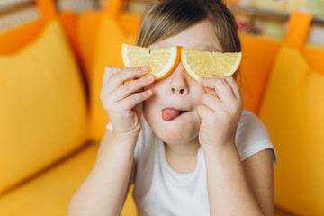 Cheerful nice pretty happy girl playing, joking with fresh orange at home in the kitchen....