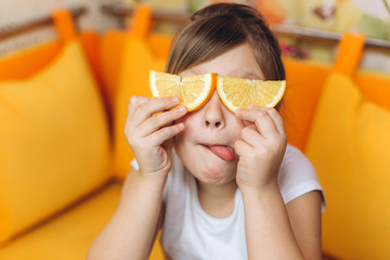 Cheerful nice pretty happy girl playing, joking with fresh orange at home in the kitchen....
