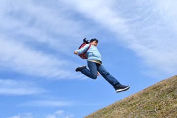 Fototapeta na wymiar 青空でジャンプする女の子（ランドセル）