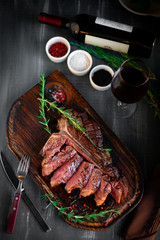 grilled sliced T-bone steak on wooden board with red wine