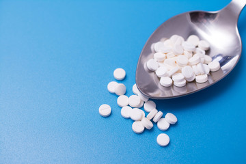 medicine tablets on a spoon isolate on blue background