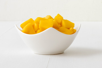 The porcelain bowl with pieces of fresh mango on the white wooden table.