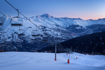 Fototapeta na wymiar La Plagne ski resort in French Savoy Alps at sunrise in winter. View of snow covered mountains, groomed ski slopes and ski lift. Mountain Mont Blanc in background
