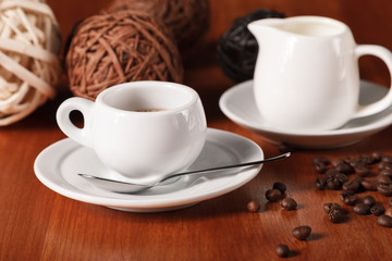 White espresso coffee Cup, coffee beans and milk jug on wooden background. Concept of coffee breaks and serving coffee