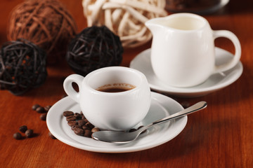 White espresso coffee Cup, coffee beans and milk jug on wooden background. Concept of coffee breaks and serving coffee